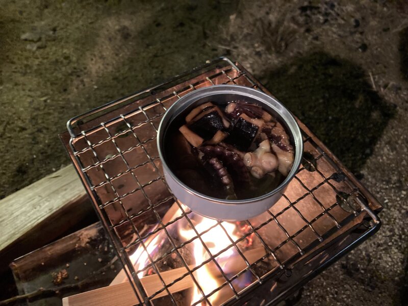 タコのオイル煮の缶詰を焚火の火であっためています。